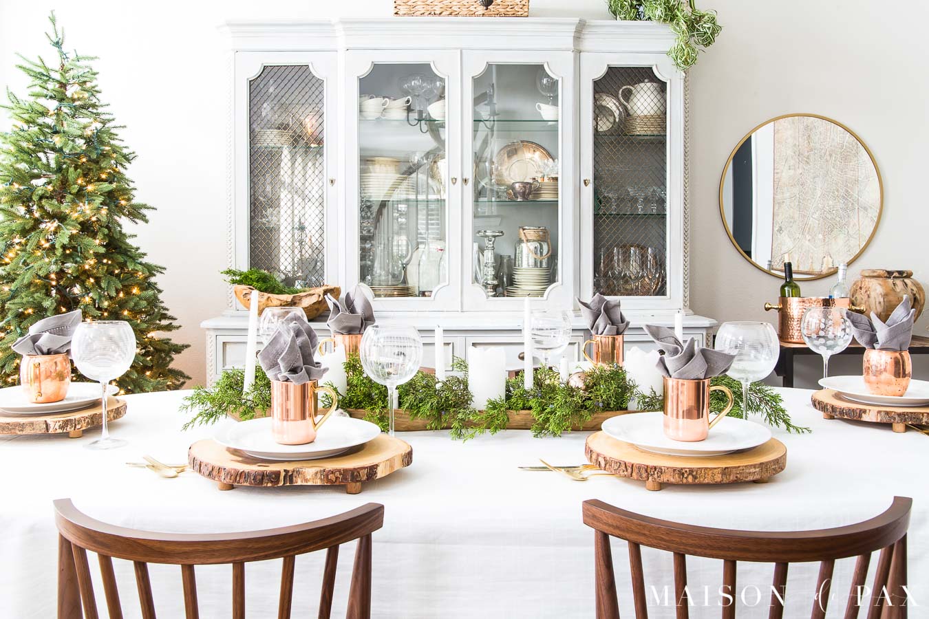 simple wooden chairs in the foreground with a dining table set with white tablecloth and holiday greenery lay beyond