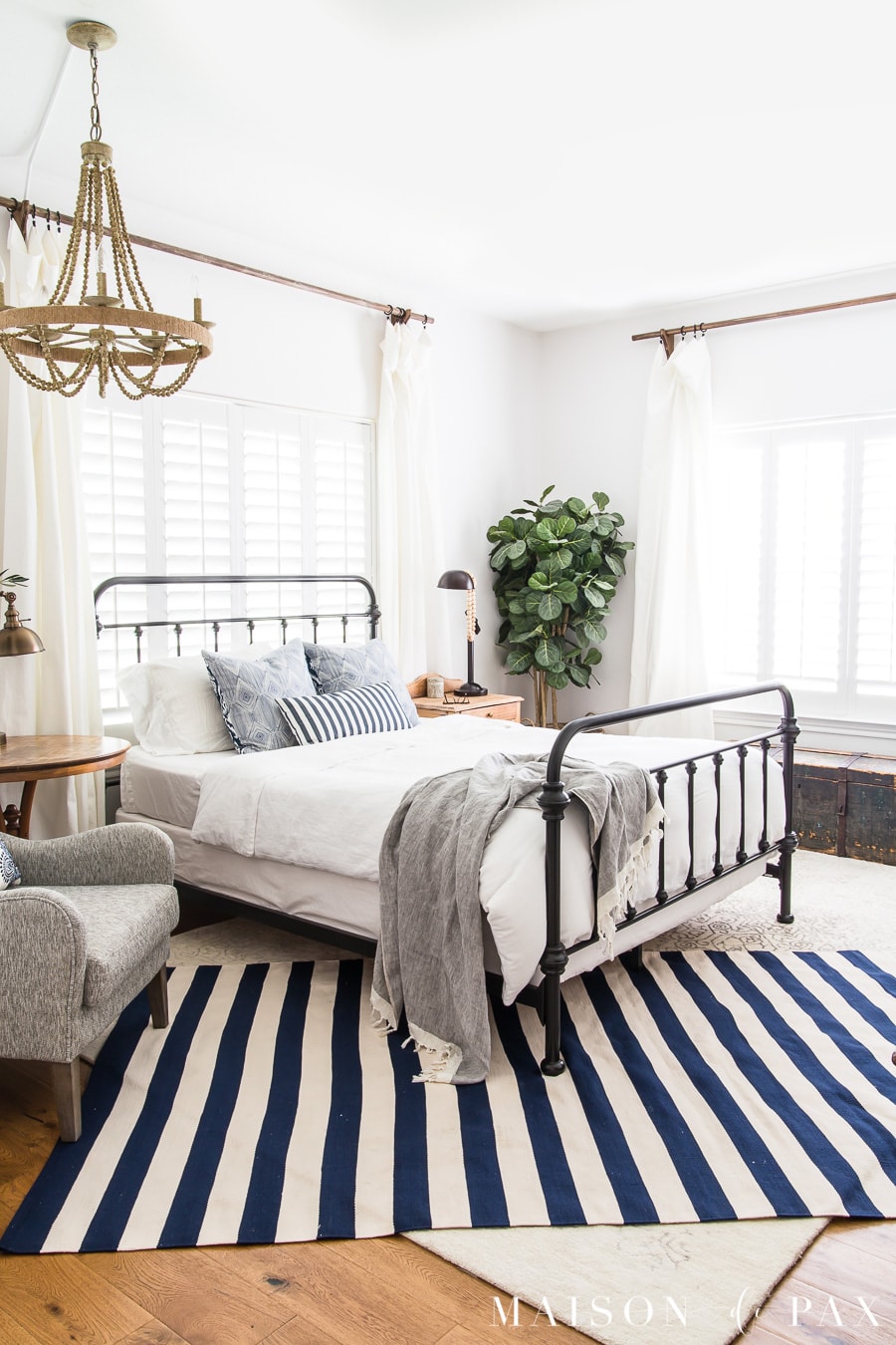 simple coastal master bedroom: get tips for casual blue and white bedroom decor! #bluewhitestripes #bedroomdecor #farmhousebedroom #ironbed #layeredrugs #bedroomdecoratingideas